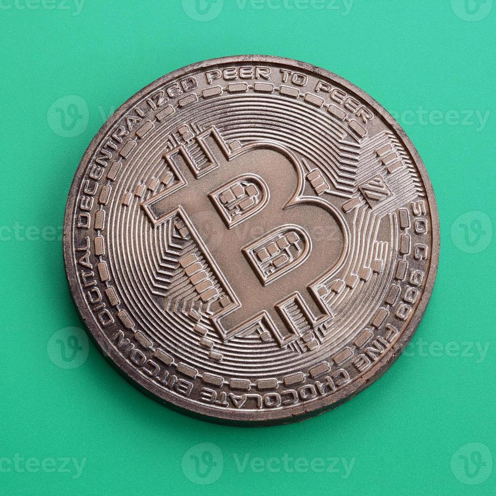 Chocolate product in the form of physical bitcoin lies on a green plastic background. Model of the crypto currency in the edible form photo