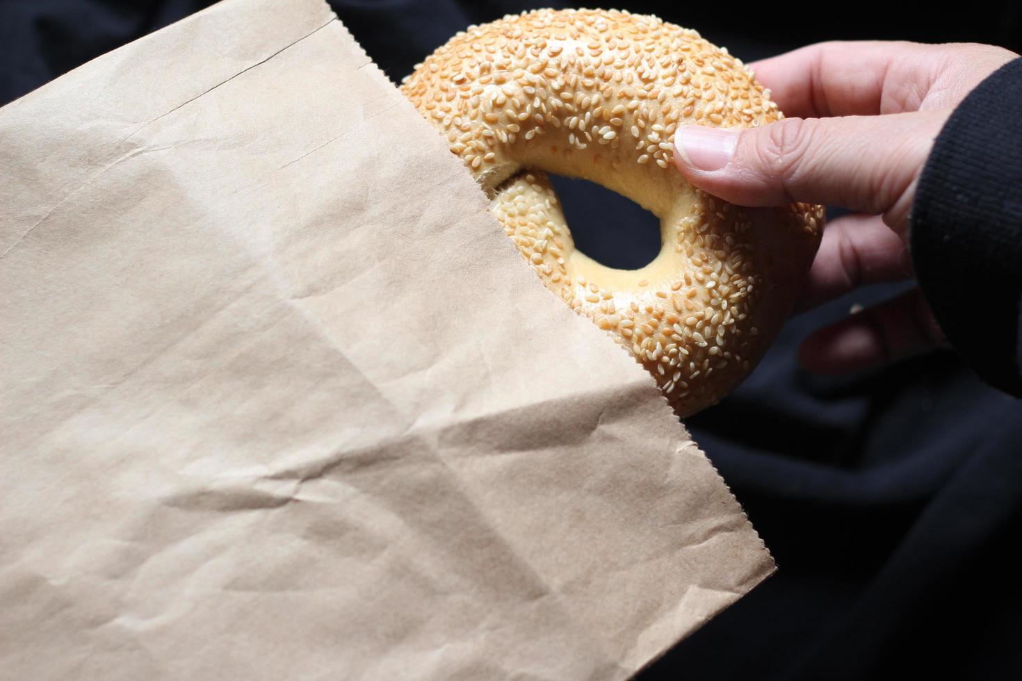 A man's hand is holding a bagel out of a brown paper bag. photo