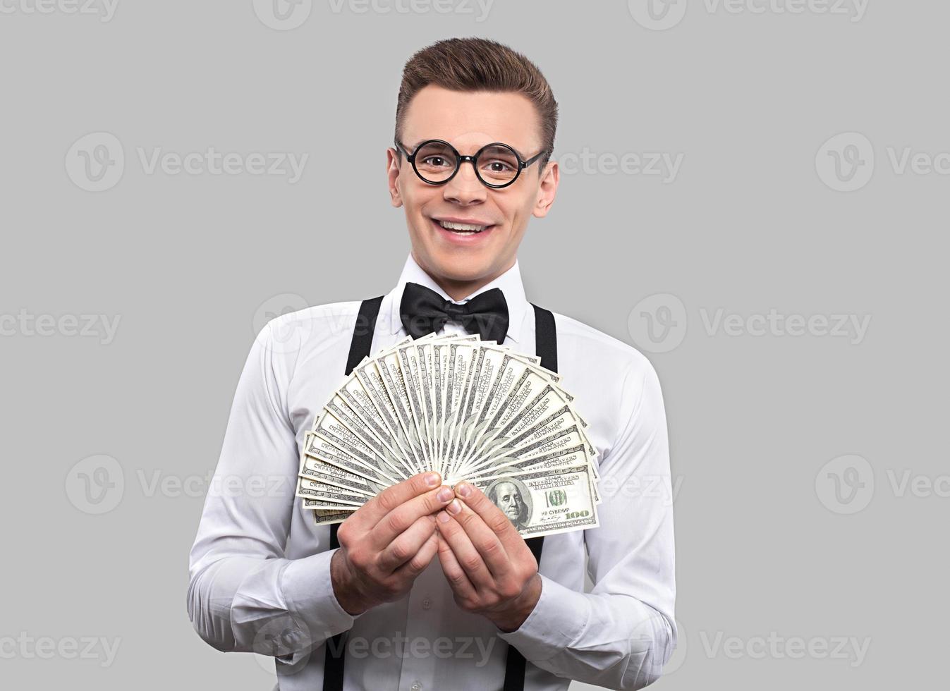 Smart and wealthy. Portrait of young nerd man in bow tie and suspenders looking at camera and gesturing while standing against grey background photo