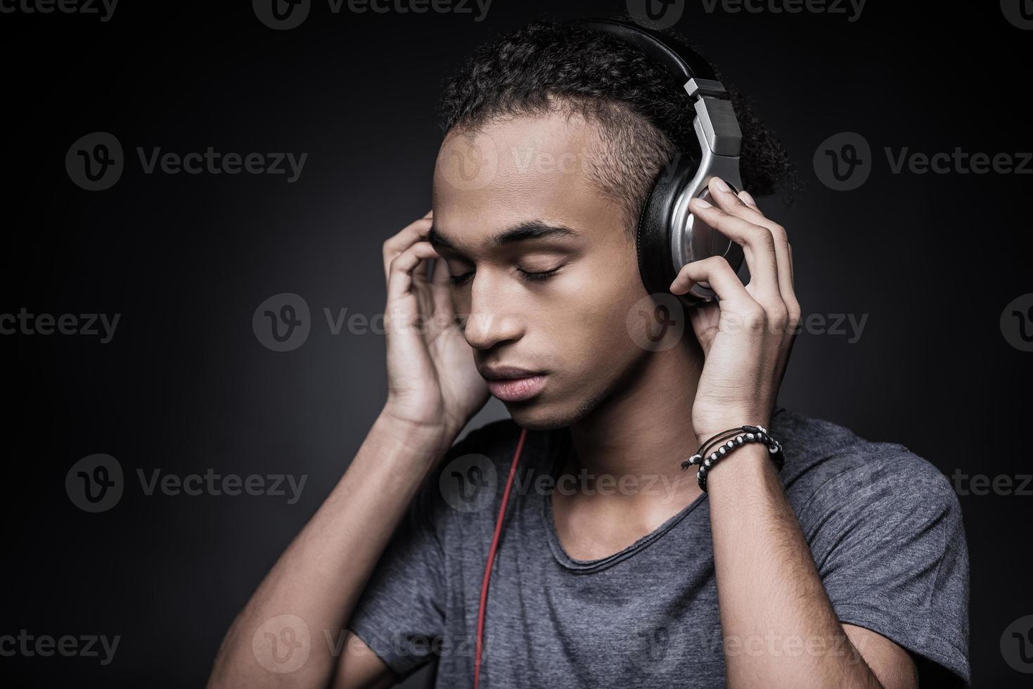 música soul. vista lateral del joven africano ajustando los auriculares y manteniendo los ojos cerrados mientras está de pie contra el fondo negro foto