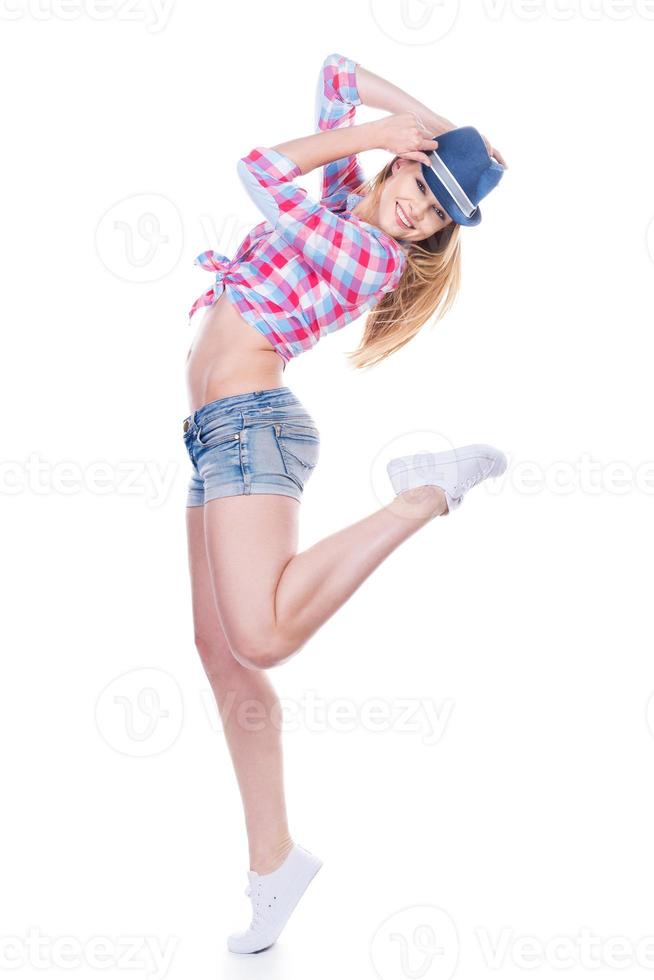 Carefree and happy. Beautiful young woman in funky wear adjusting her hat and looking at camera while standing against white background photo