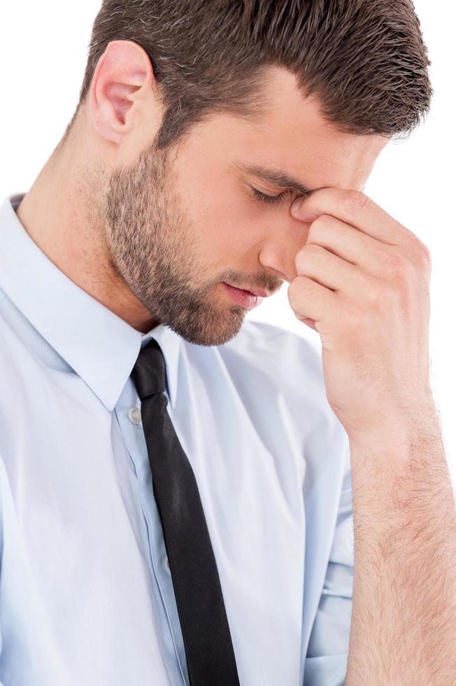 Feeling exhausted. Side view of young man in shirt and tie touching his nose with fingers and keeping eyes closed while standing isolated on white background photo