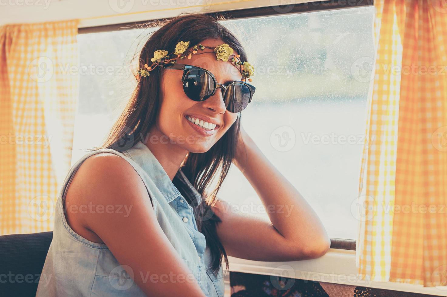 Flower child in the sun. Happy young woman smiling at camera while sitting inside of the retro van photo