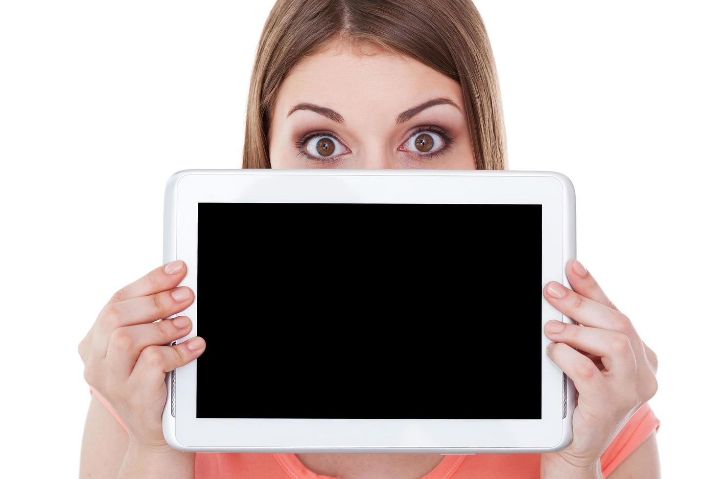 Copy space on her digital tablet. Surprised young woman looking out of the digital tablet while standing isolated on white photo