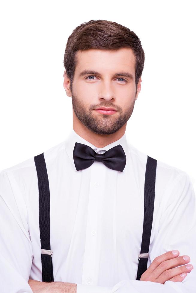 encantador guapo. retrato de un joven confiado con camisa blanca y corbata de moño con los brazos cruzados y mirando a la cámara mientras está aislado en blanco foto