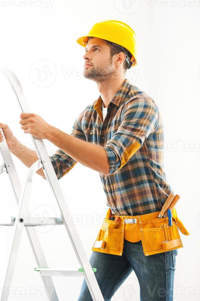 Climbing his way to the top. Confident young craftsperson climbing up the ladder and looking up photo