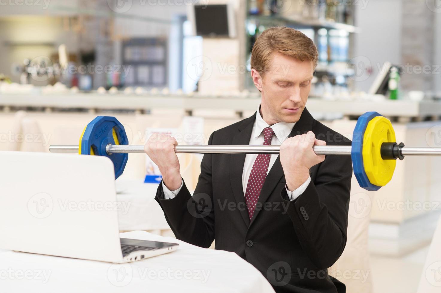 I choose healthy lifestyle. Confident young red hair man in formalwear sitting at the restaurant and holding a dumbbell photo