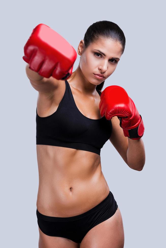 Woman boxing. Beautiful young sporty woman boxing while standing against grey background photo