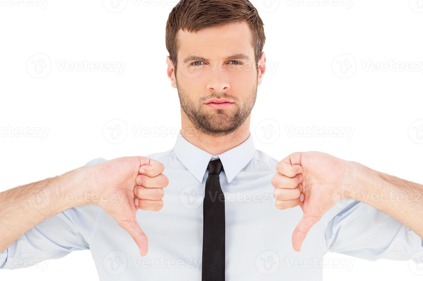 Rejected Portrait of confident young man in shirt and tie looking at camera and showing his thumbs down while standing isolated on white background photo