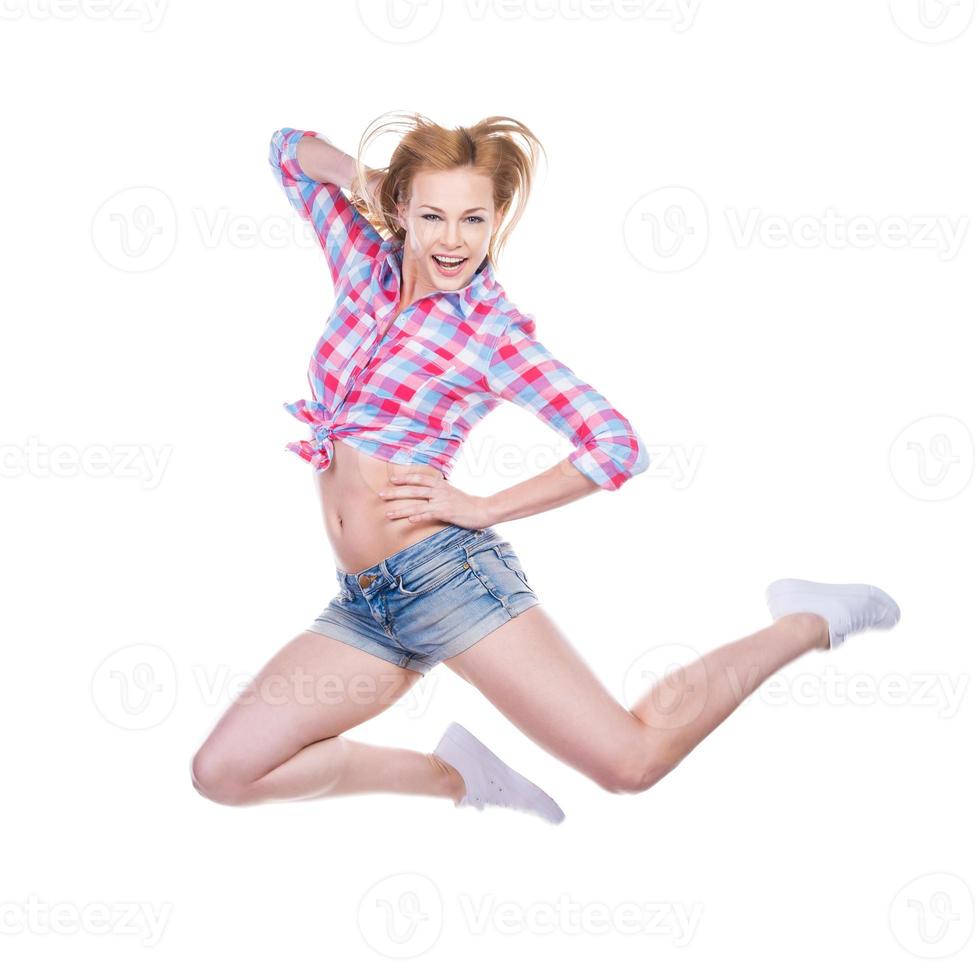 Living an active life. Attractive young woman in funky wear smiling and looking at camera while jumping against white background photo