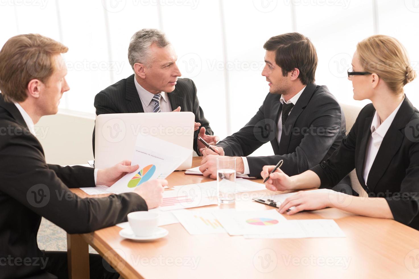 Hot discussion. Four business people in formalwear discussing something while sitting together at the meeting photo