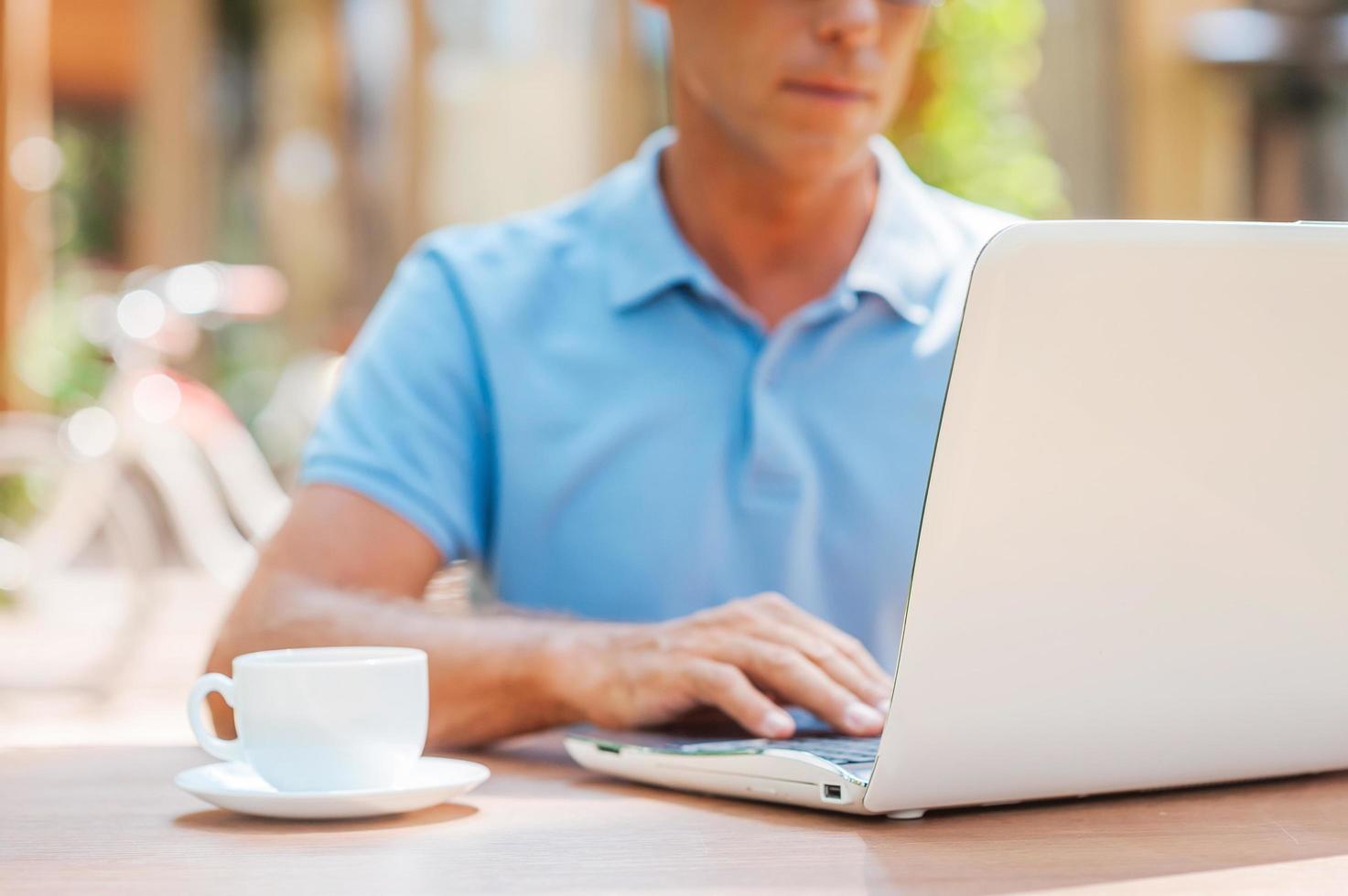 Surfing the net in cafe. Close-up of confident mature man writing something in his note pad and smiling while sitting at the table outdoors with house in the background photo