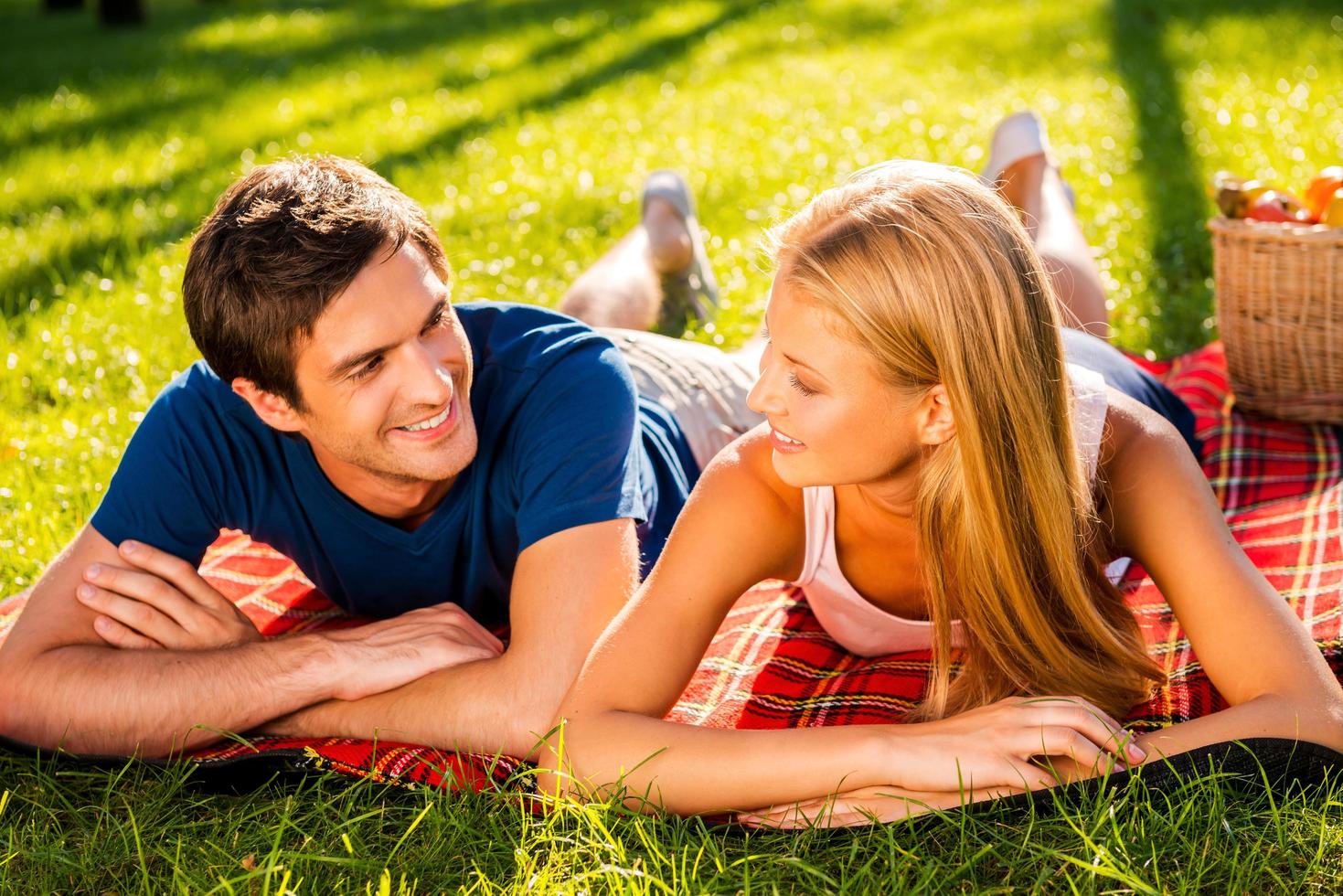 disfrutando juntos de su cita perfecta. feliz joven pareja amorosa relajándose juntos en el parque mientras están acostados en una manta de picnic y mirándose el uno al otro foto