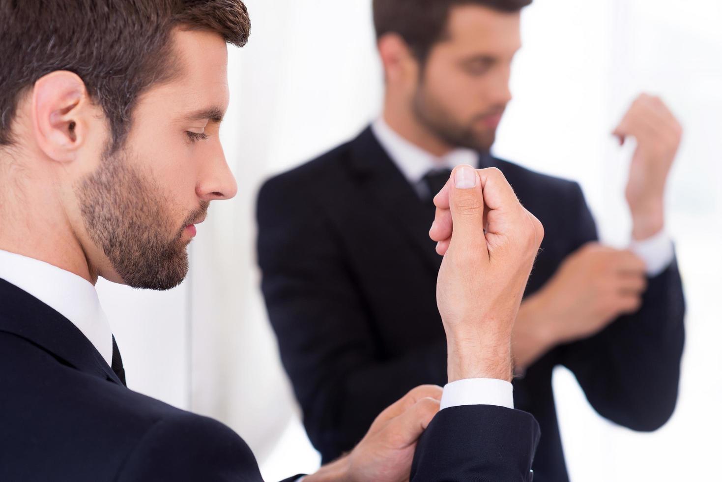 Adjusting his sleeves. Confident young man in formalwear adjusting his sleeves while standing against mirror photo