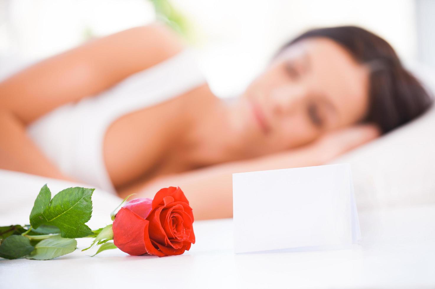 Message from boyfriend. Side view of beautiful young woman lying in bed with red rose photo