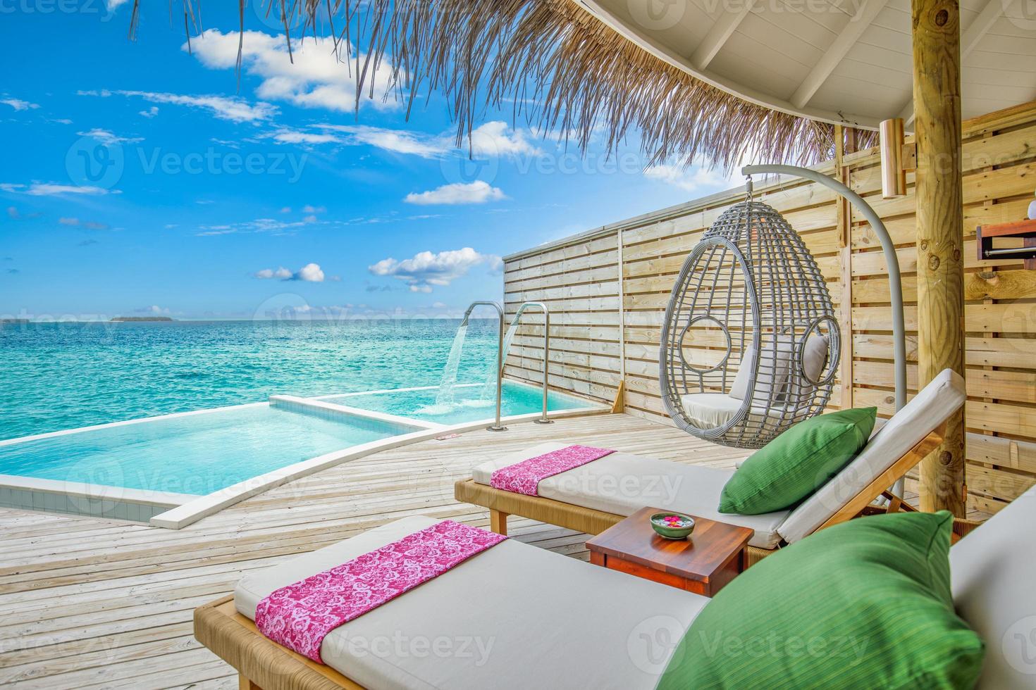 Fantastic over water villa, terrace view with sun beds chairs under umbrella, luxury pool hotel with stunning ocean view. Beautiful spa or wellness concept, recreational vacation resort tranquil area photo