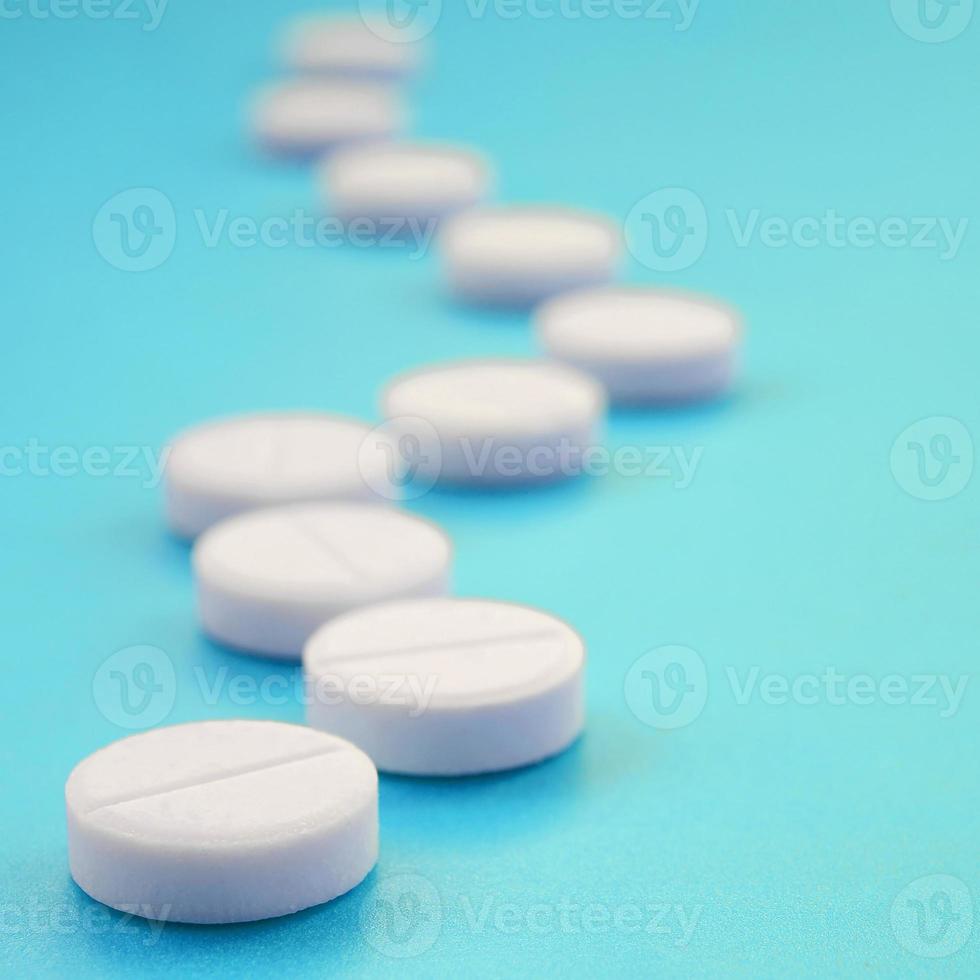 A few white tablets lie on a bright blue background surface. Background image on medical and pharmaceutical topics photo