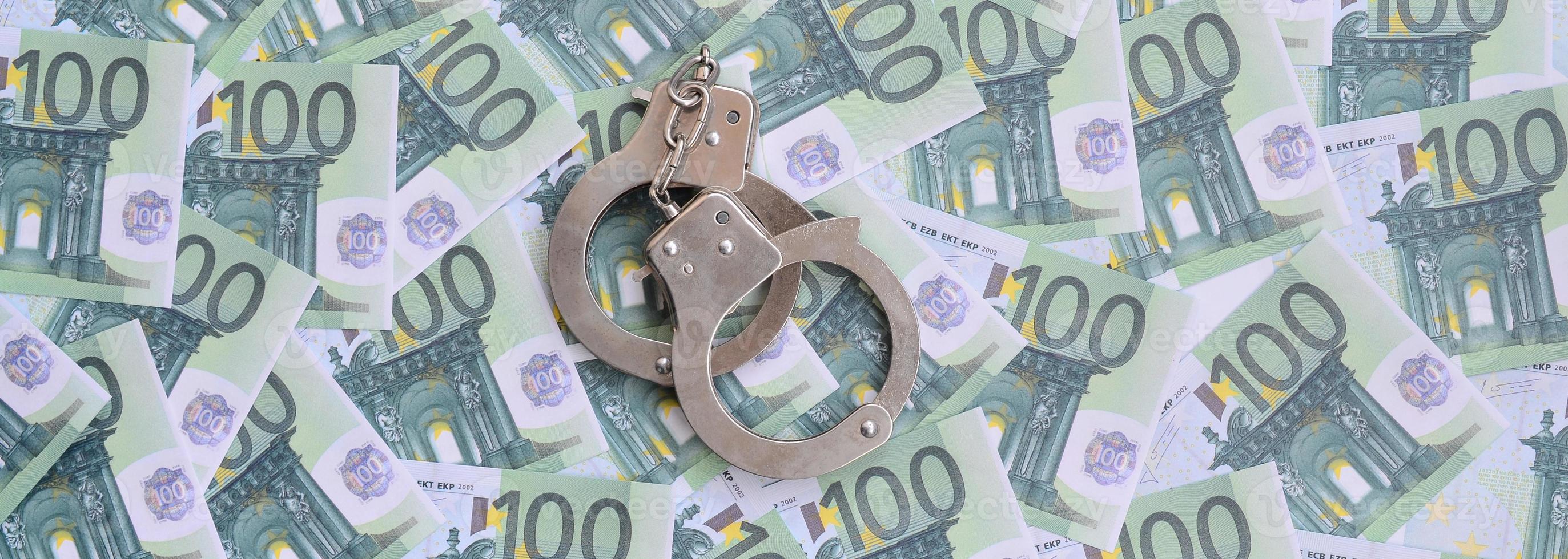 Police handcuffs lies on a set of green monetary denominations of 100 euros. A lot of money forms an infinite heap photo