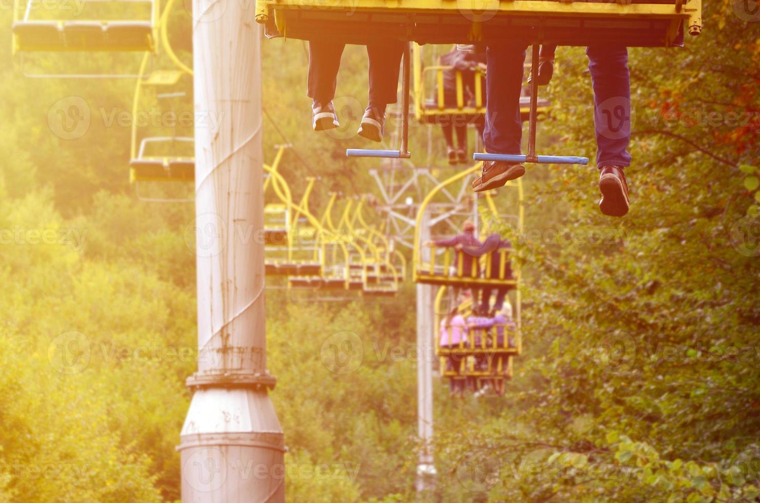 People ride on a cable car. The legs of passengers hang over the mountain forest photo