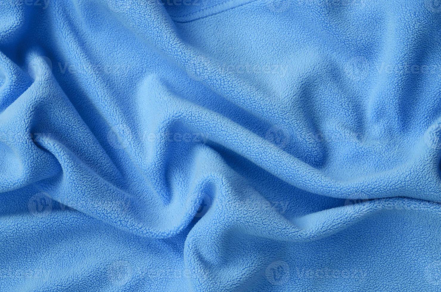 The blanket of furry blue fleece fabric. A background of light blue soft plush fleece material with a lot of relief folds photo
