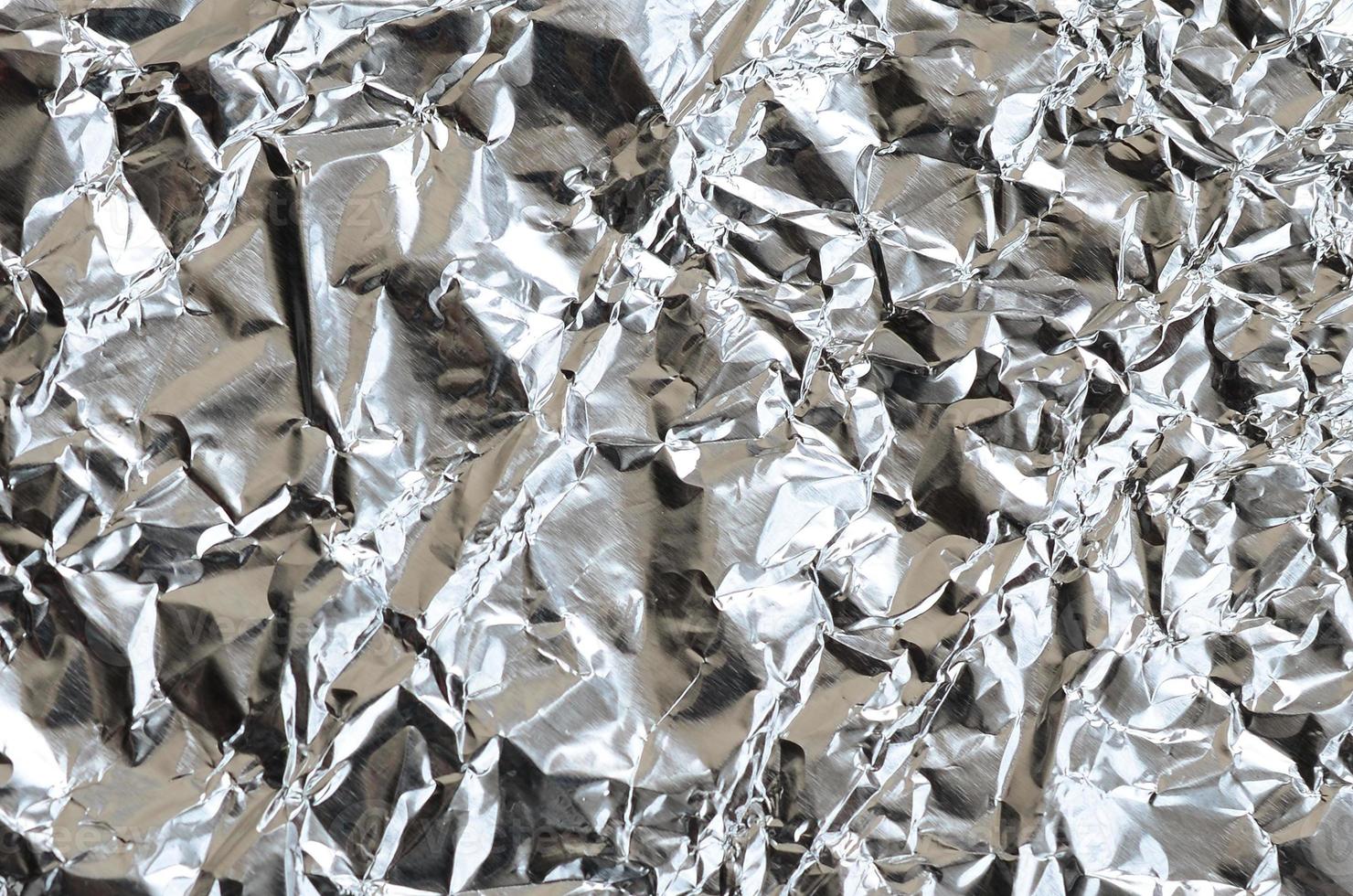 Thin wrinkled sheet of crushed tin aluminum silver foil background with shiny crumpled surface for texture photo