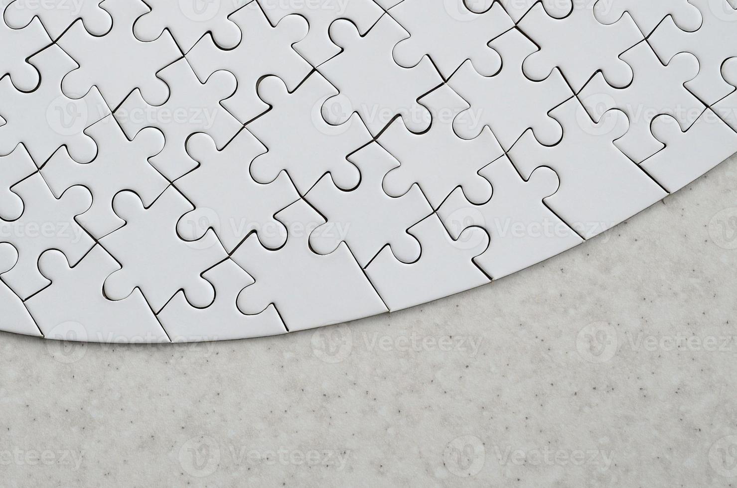A white jigsaw puzzle in the complete form lies on a treated stone surface. Textured image with copy space photo