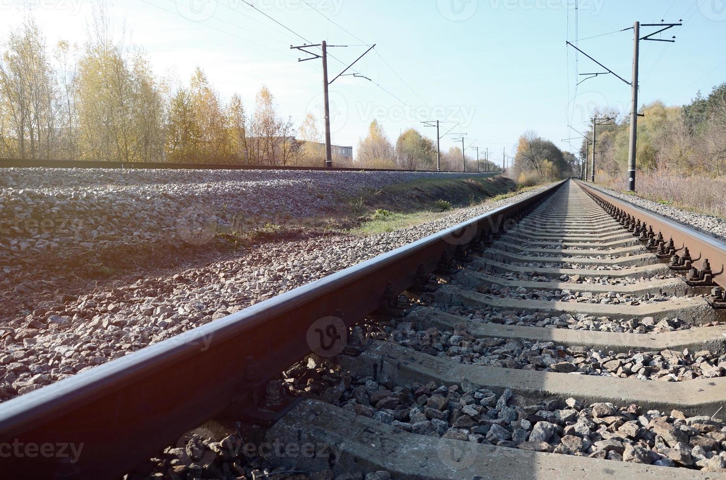 Autumn industrial landscape. Railway receding into the distance among green and yellow autumn trees photo