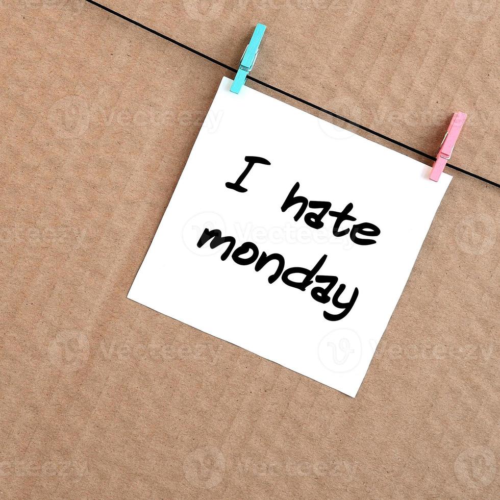 I hate monday. Note is written on a white sticker that hangs with a clothespin on a rope on a background of brown cardboard photo