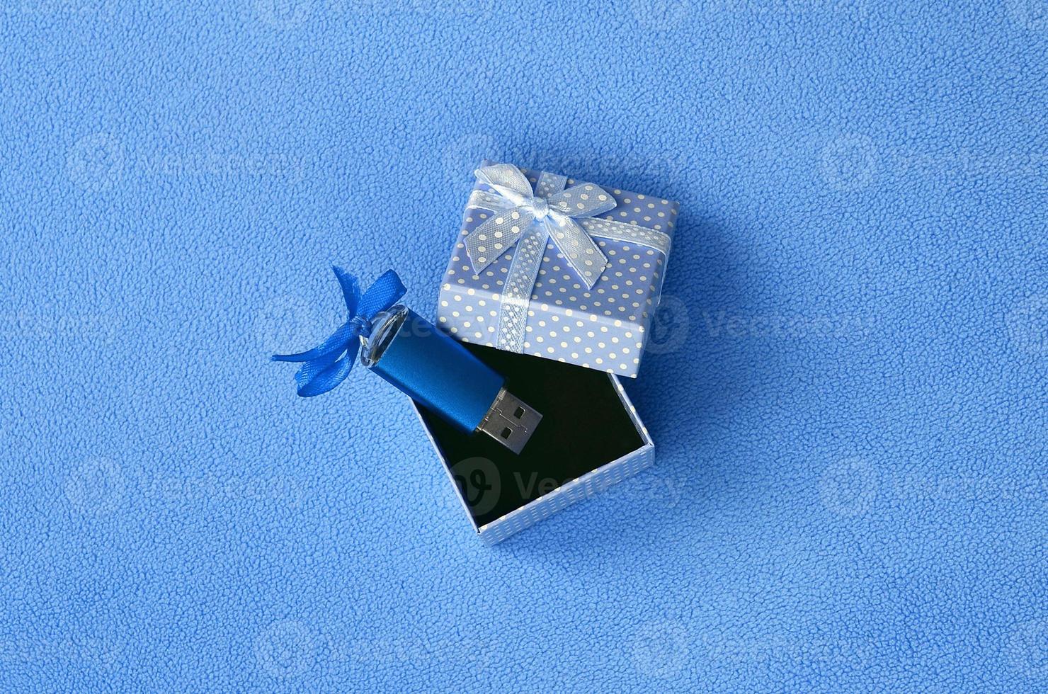 Brilliant blue usb flash memory card with a blue bow lies in a small gift box in blue with a small bow on a blanket of soft and furry light blue fleece fabric. Classic female gift memory card design photo