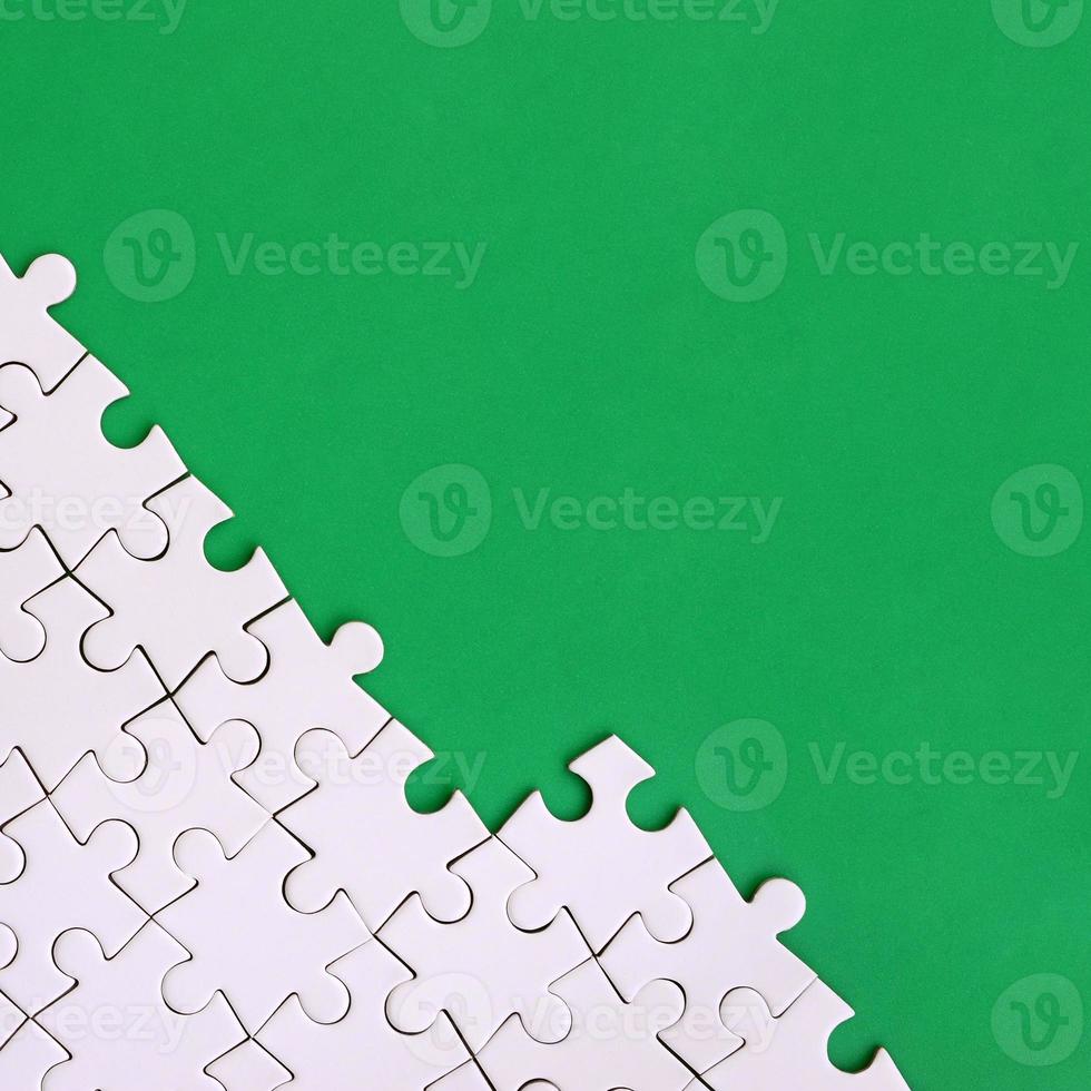 Fragment of a folded white jigsaw puzzle on the background of a green plastic surface. Texture photo with copy space for text