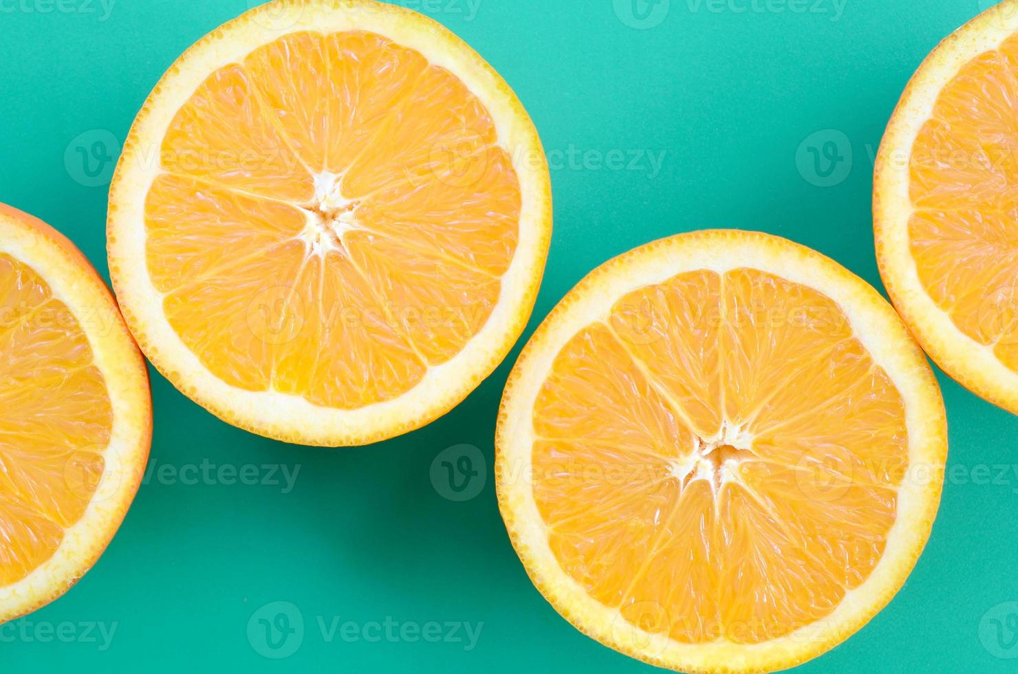 Top view of a several orange fruit slices on bright background in turquoise green color. A saturated citrus texture image photo