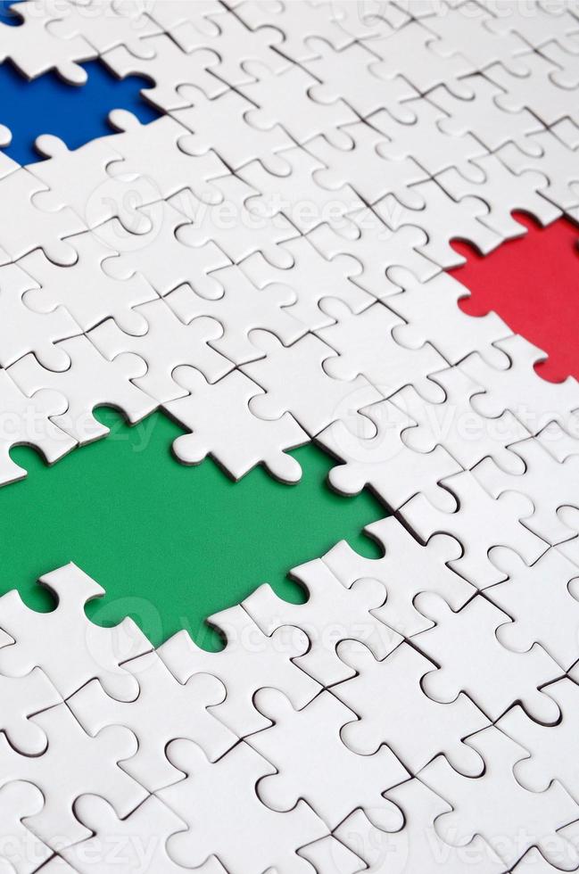 Close-up texture of a white jigsaw puzzle in assembled condition with missing elements, under which surfaces of different colors photo