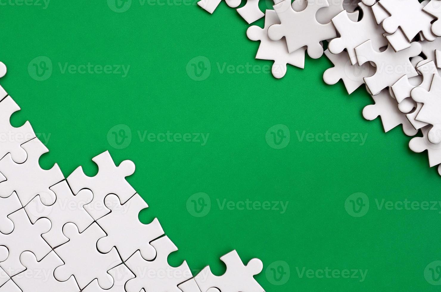 Fragment of a folded white jigsaw puzzle and a pile of uncombed puzzle elements against the background of a green surface. Texture photo with space for text