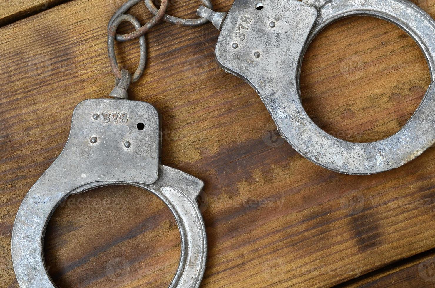 Old and rusty police handcuffs lie on a scratched wooden surface. The concept of an old crime photo