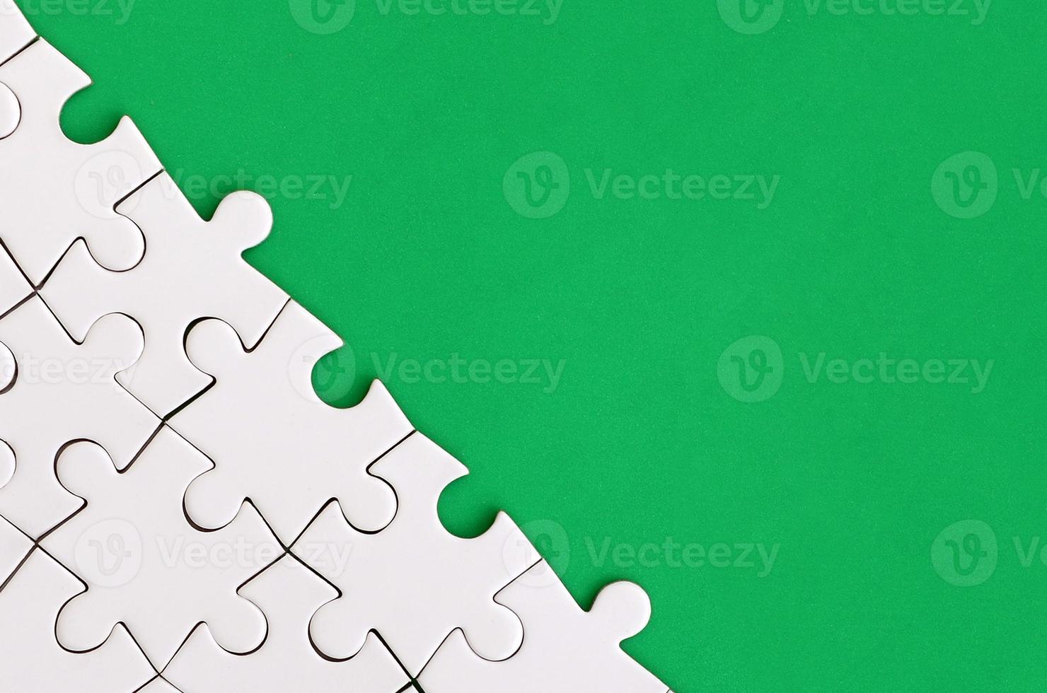 Fragment of a folded white jigsaw puzzle on the background of a green plastic surface. Texture photo with copy space for text