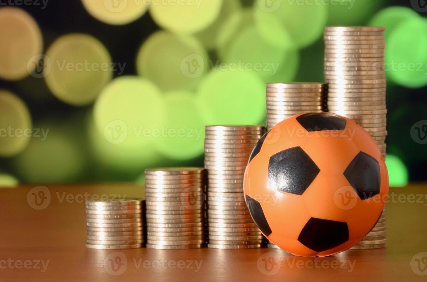 Soccer ball and stacks of golden coins in growth graph on the blurred bokeh background photo