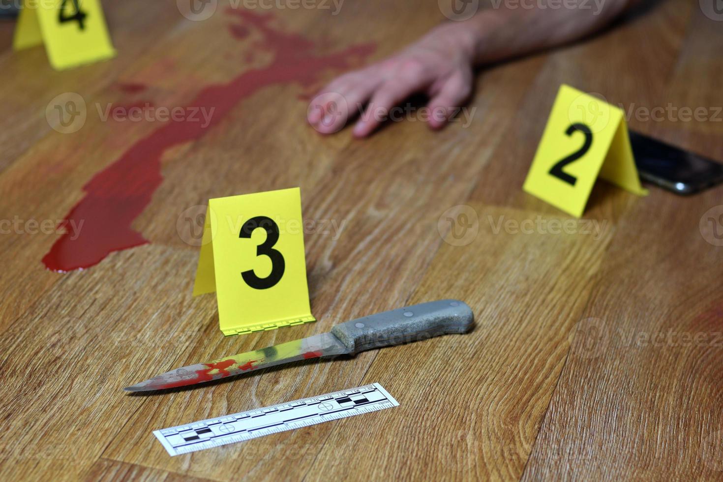 Crime scene investigation - Bloody knife and victims hand with yellow criminal markers on kitchen floor photo