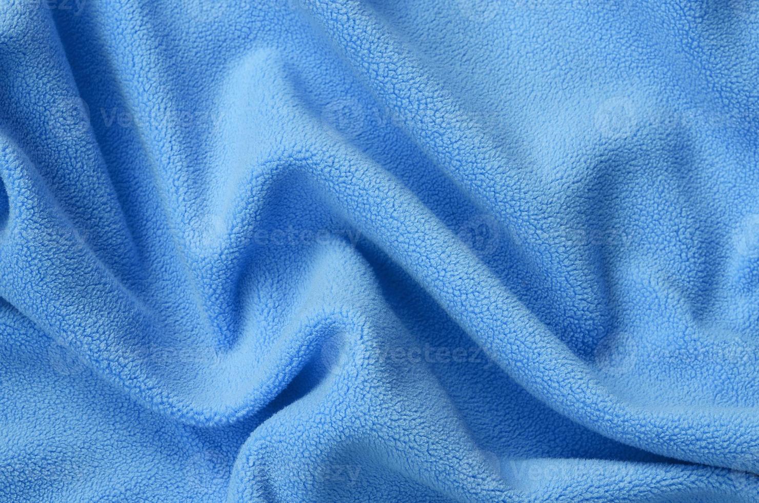 The blanket of furry blue fleece fabric. A background of light blue soft plush fleece material with a lot of relief folds photo