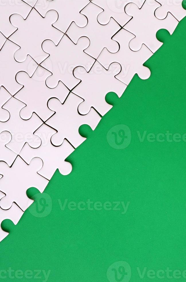 Fragment of a folded white jigsaw puzzle on the background of a green plastic surface. Texture photo with copy space for text