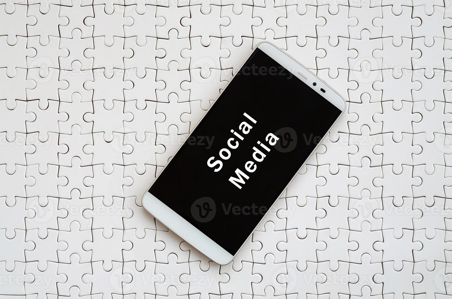 A modern big smartphone with a touch screen lies on a white jigsaw puzzle in an assembled state with inscription. Social media photo