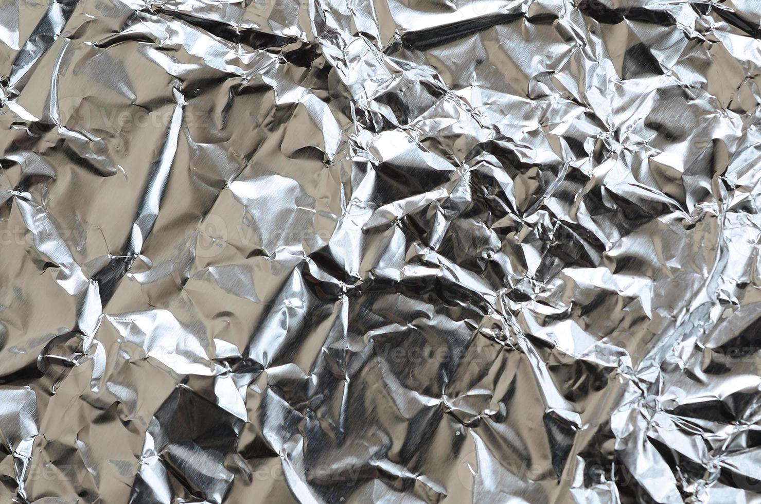 Thin wrinkled sheet of crushed tin aluminum silver foil background with shiny crumpled surface for texture photo