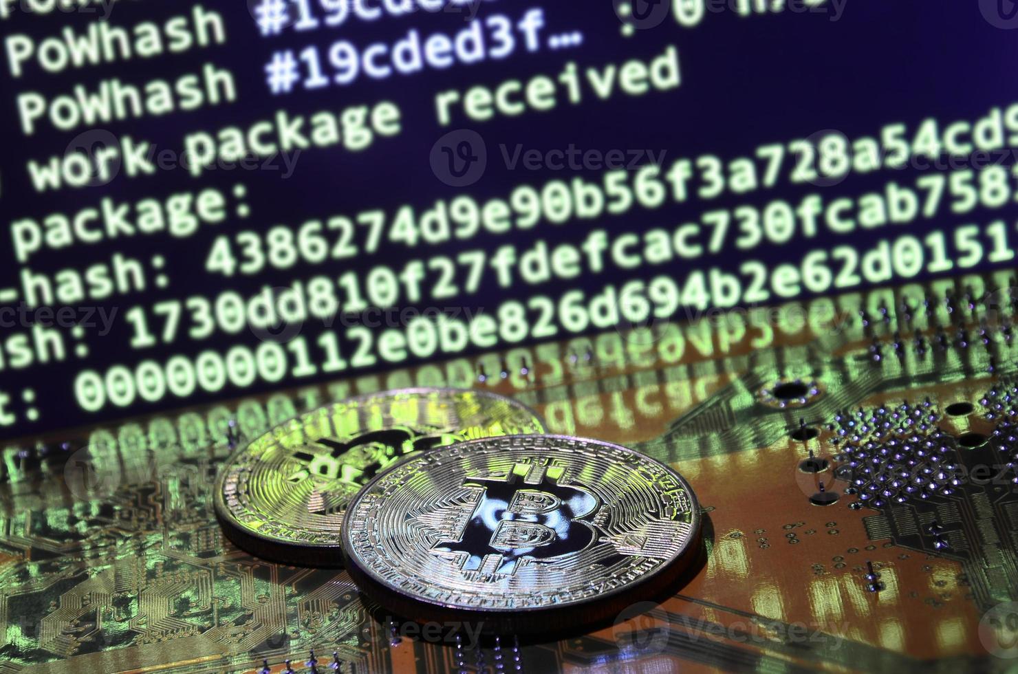 Two bitcoins lies on a videocard surface with background of screen display of cryptocurrency mining by using the GPUs photo