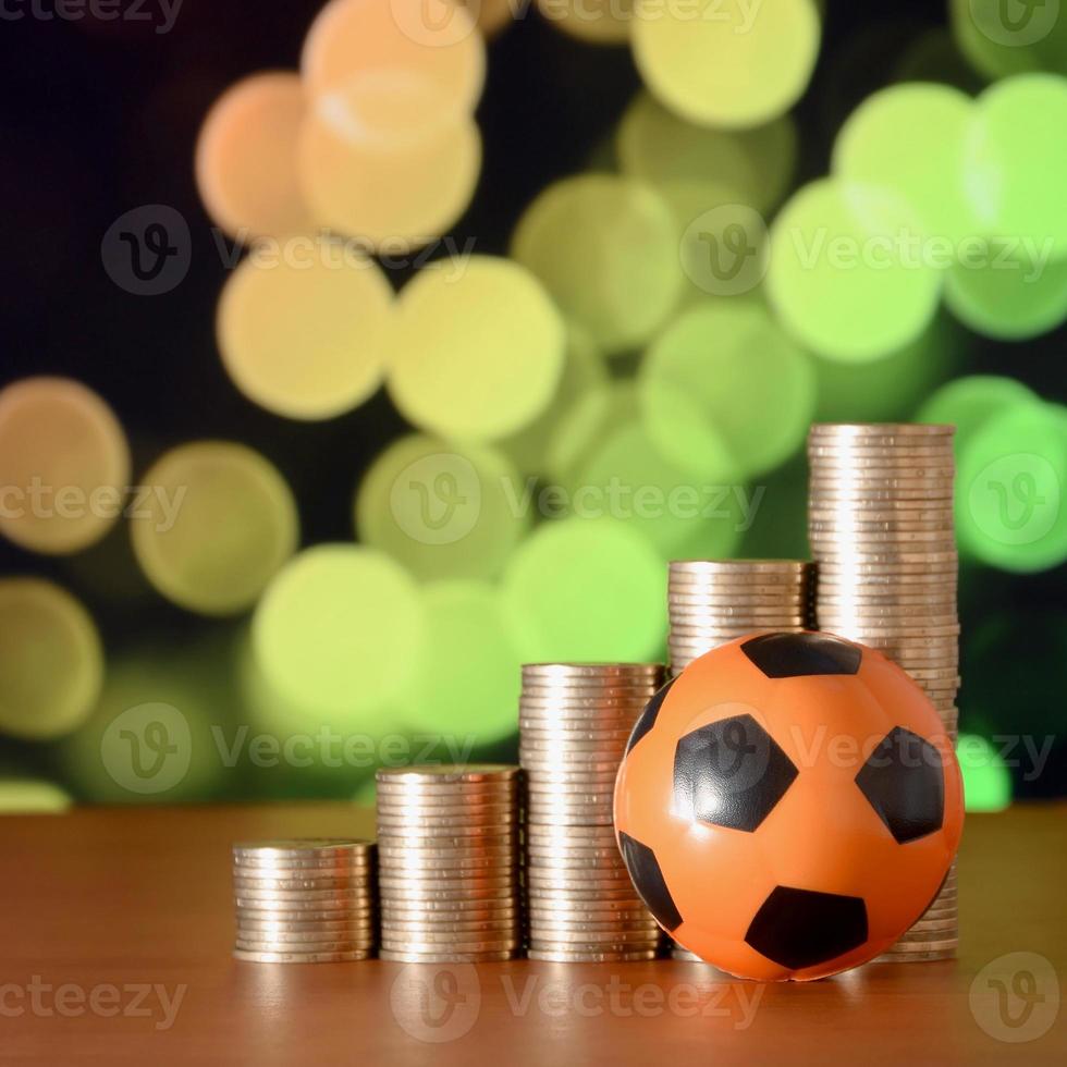 Soccer ball and stacks of golden coins in growth graph on the blurred bokeh background photo