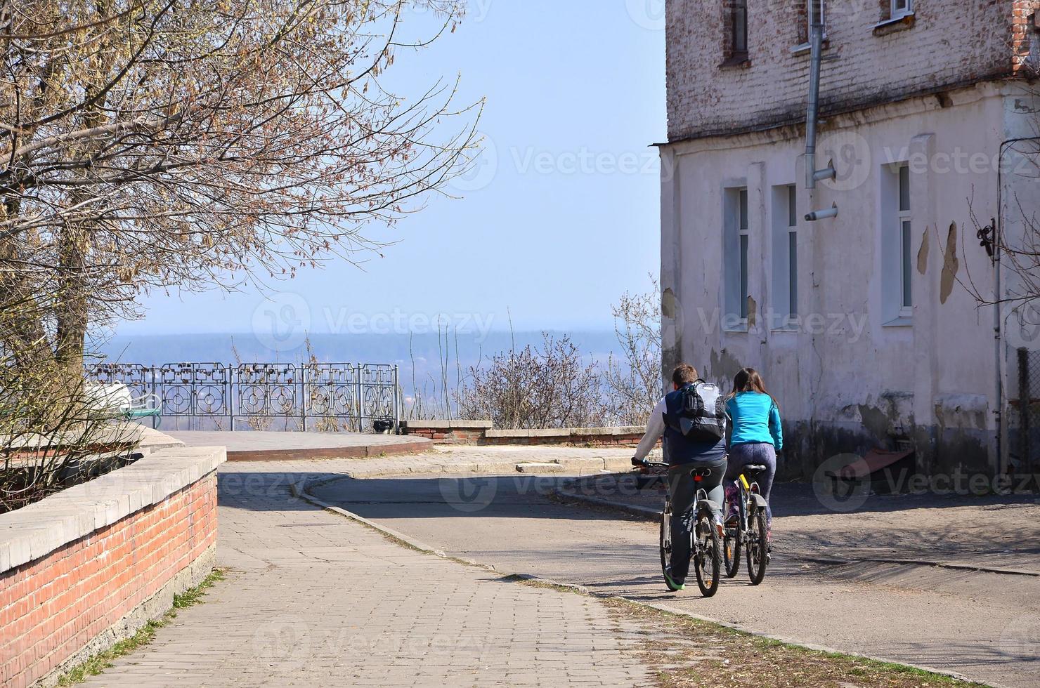 A young couple of bikers ride through empty streets during clear weather. The guy and the girl go on bicycles photo