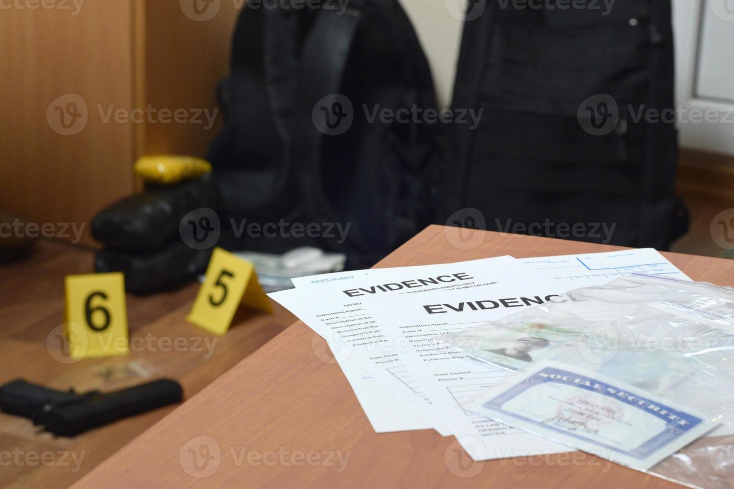 Evidence Labels and green card with ssn number lies on table with big amount of items as evidence in crime scene investigation process on backdrop photo