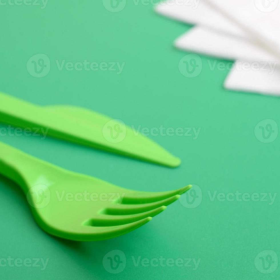 Disposable plastic cutlery green. Plastic fork and knife lie on a green background surface next to napkins photo