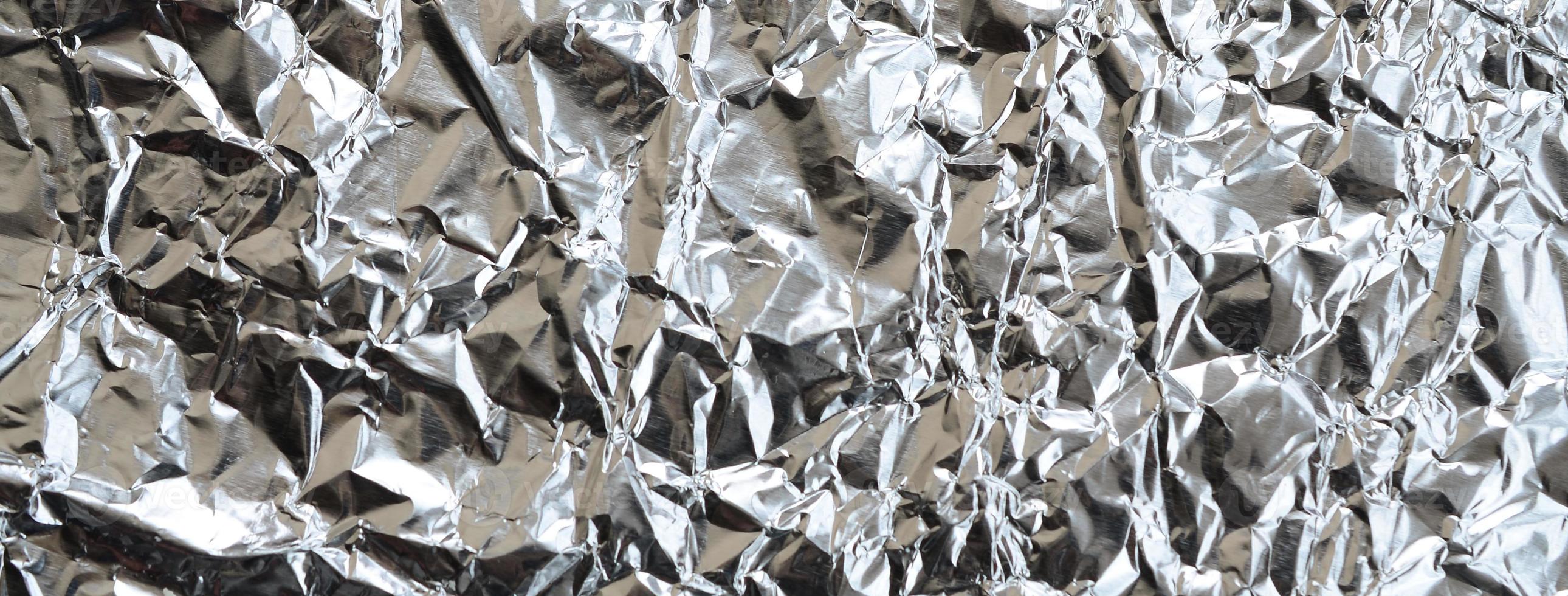 Thin wrinkled sheet of crushed tin aluminum silver foil background with shiny crumpled surface for texture photo
