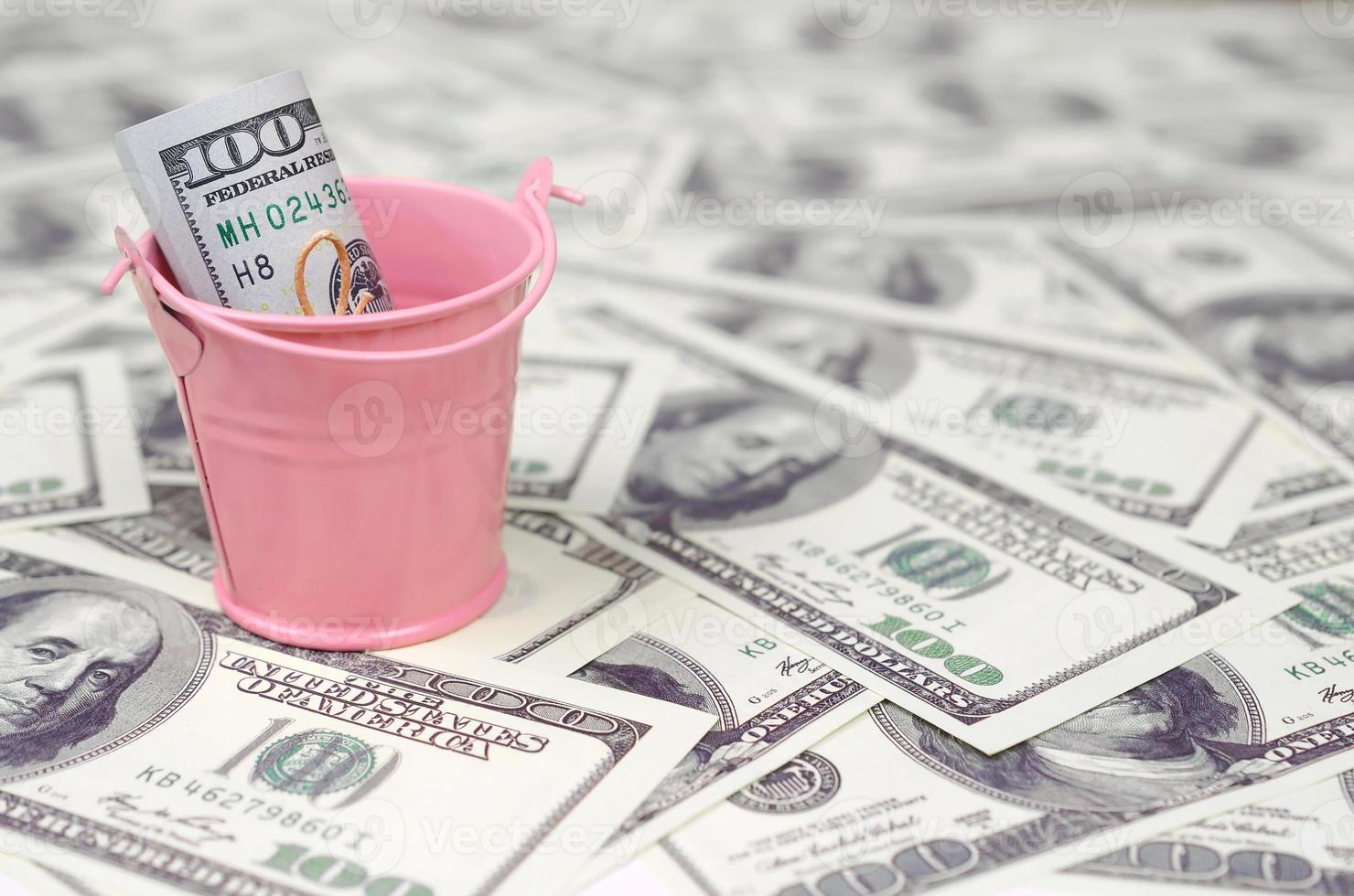 A bundle of US dollars in a metal pink bucket on a set of dollar bills photo