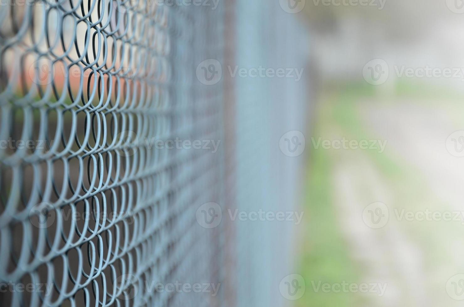 A photograph of a metal net used as a fence of private possessions. Old metal grid in perspective with a blurred background photo