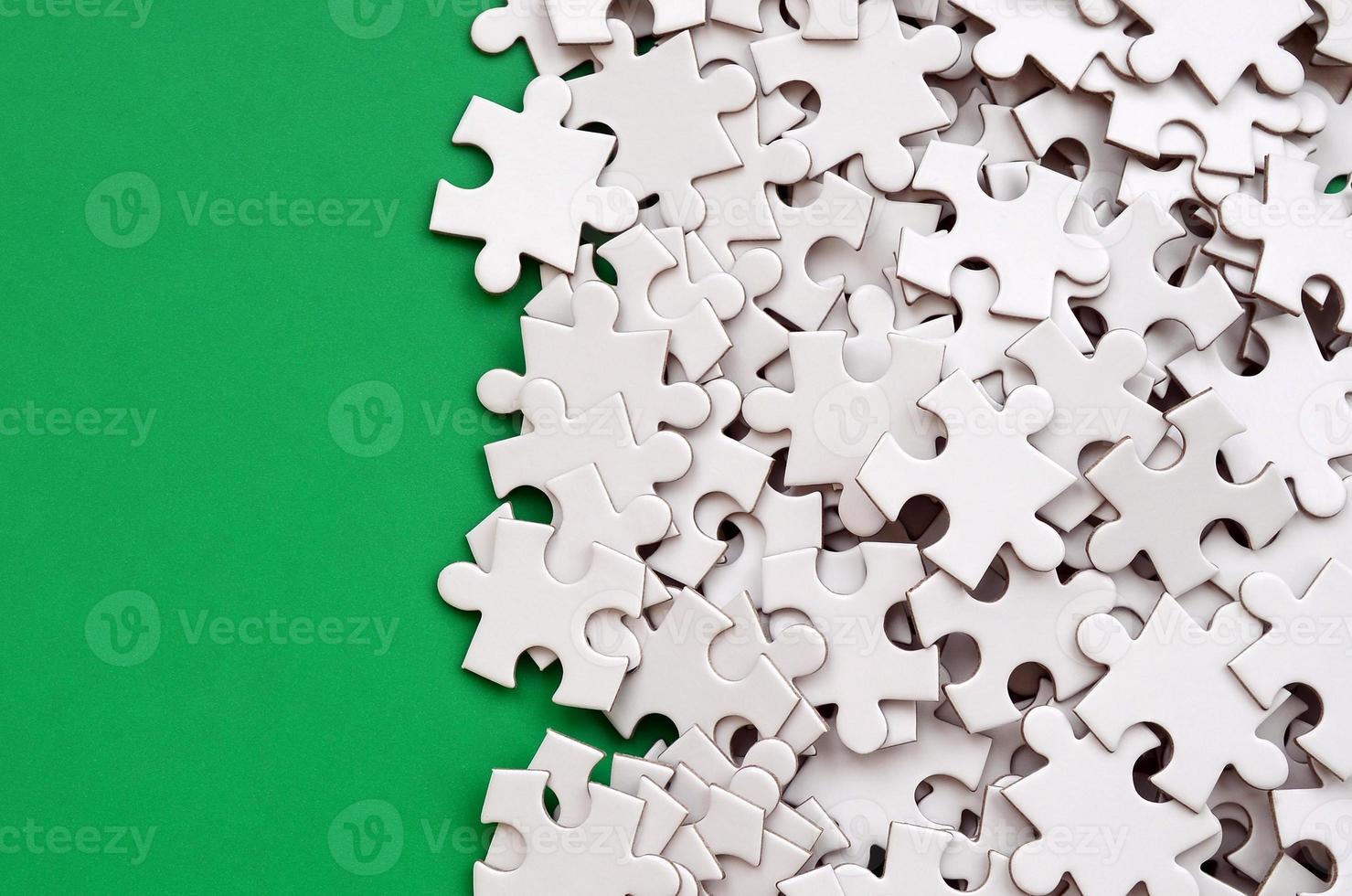 A pile of uncombed elements of a white jigsaw puzzle lies on the background of a green surface. Texture photo with copy space for text